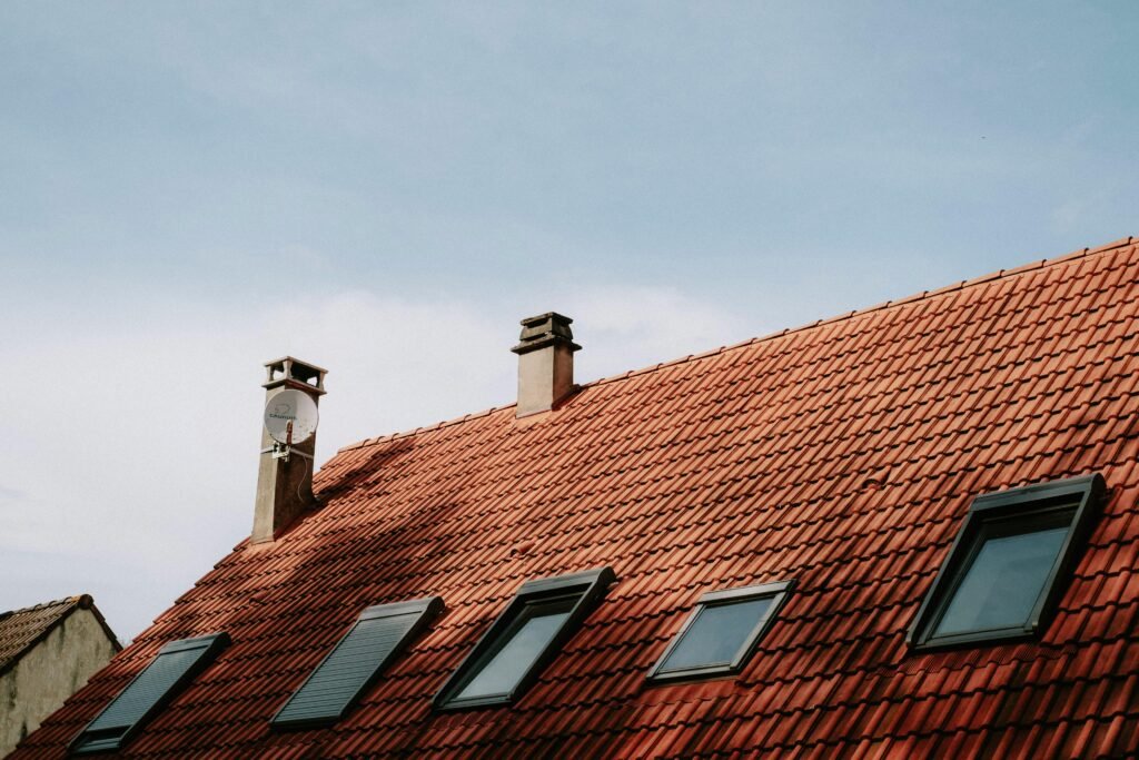 metal-roof A picturesque red tiled roof featuring chimneys and skylight windows against a blue sky.