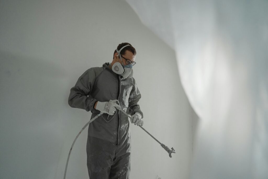 metal-roof-1 Person in protective gear painting a wall, showcasing house renovation work.