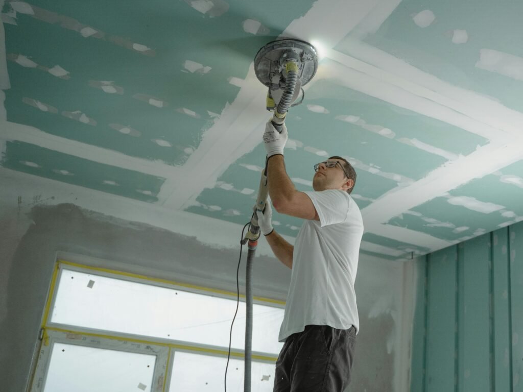 services-1 A professional worker sanding the ceiling during a home renovation project. Indoor construction setting.